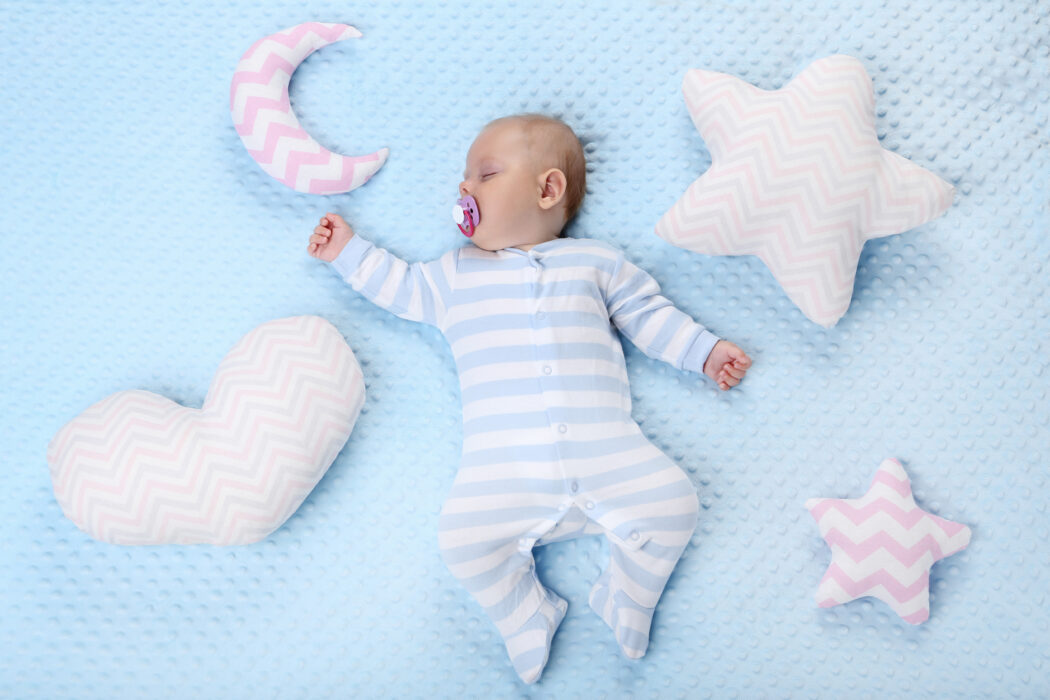 baby nachts anziehen säugling mit schnuller schläft im schlafanzug auf blauer decke mit kuschelkissen