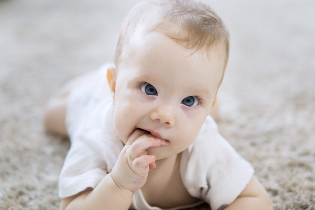kleines baby schielt liegt auf dem bauch finger im mund