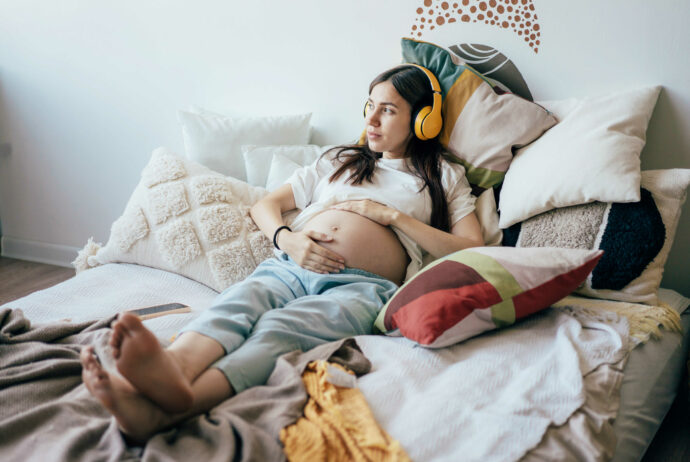 bettruhe schwangerschaft frau mit babybauch liegt mit kopfhörer in bunten kissen