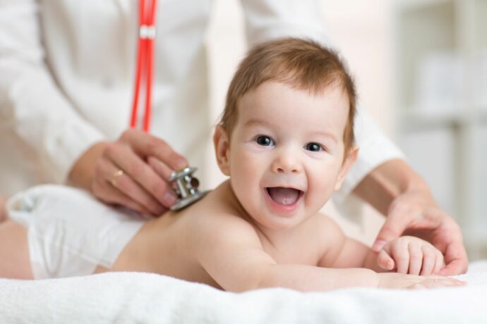 lachendes baby liegt fuer u-untersuchungen beim kinderarzt zum abhoeren auf dem bauch