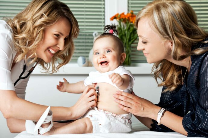 lachendes baby wird beim kinderarzt abgehört sitzt zwischen mutter und kinderärztin