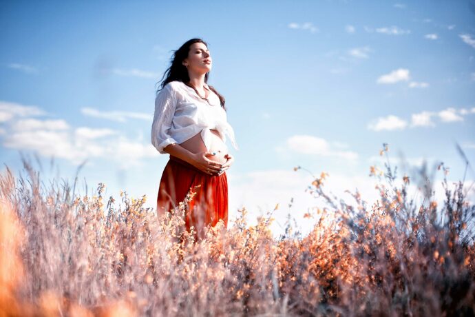 frau konnte erfolgreich schwanger werden nach fehlgeburt steht mit geschlossenen augen auf feld und hält babybauch mit händen